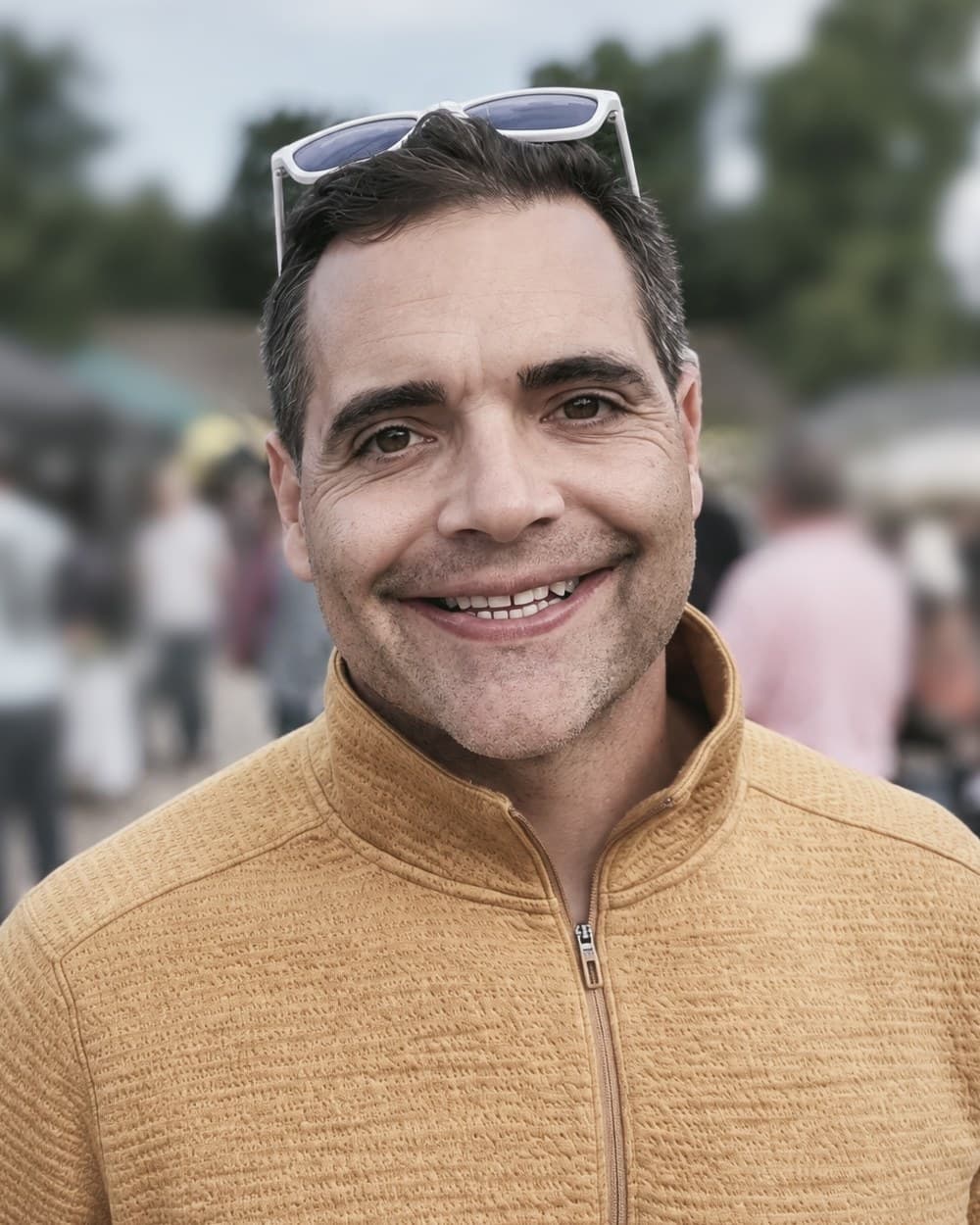 Dr. Steven K. LeGault, DC, smiling outdoors in a mustard-yellow quarter-zip, sunglasses resting on his head